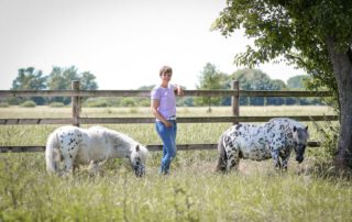 Katharina Hülsken steht am Zaun, während ihre Ponys selbstständig grasen – Delegieren lernen und als Führungskraft loslassen